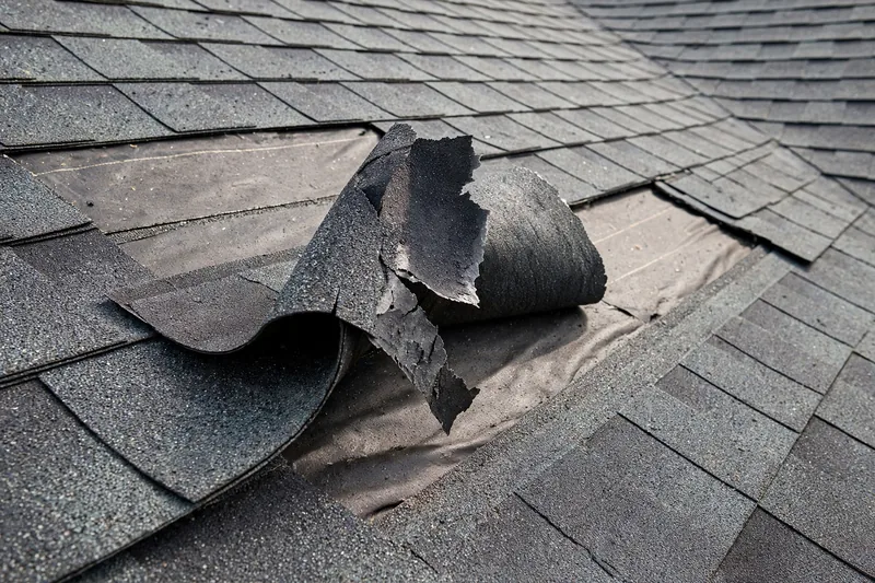 Wind-lifted asphalt shingle tabs with broken seal strips on an Owasso roof after a spring storm — the classic straight-line wind signature